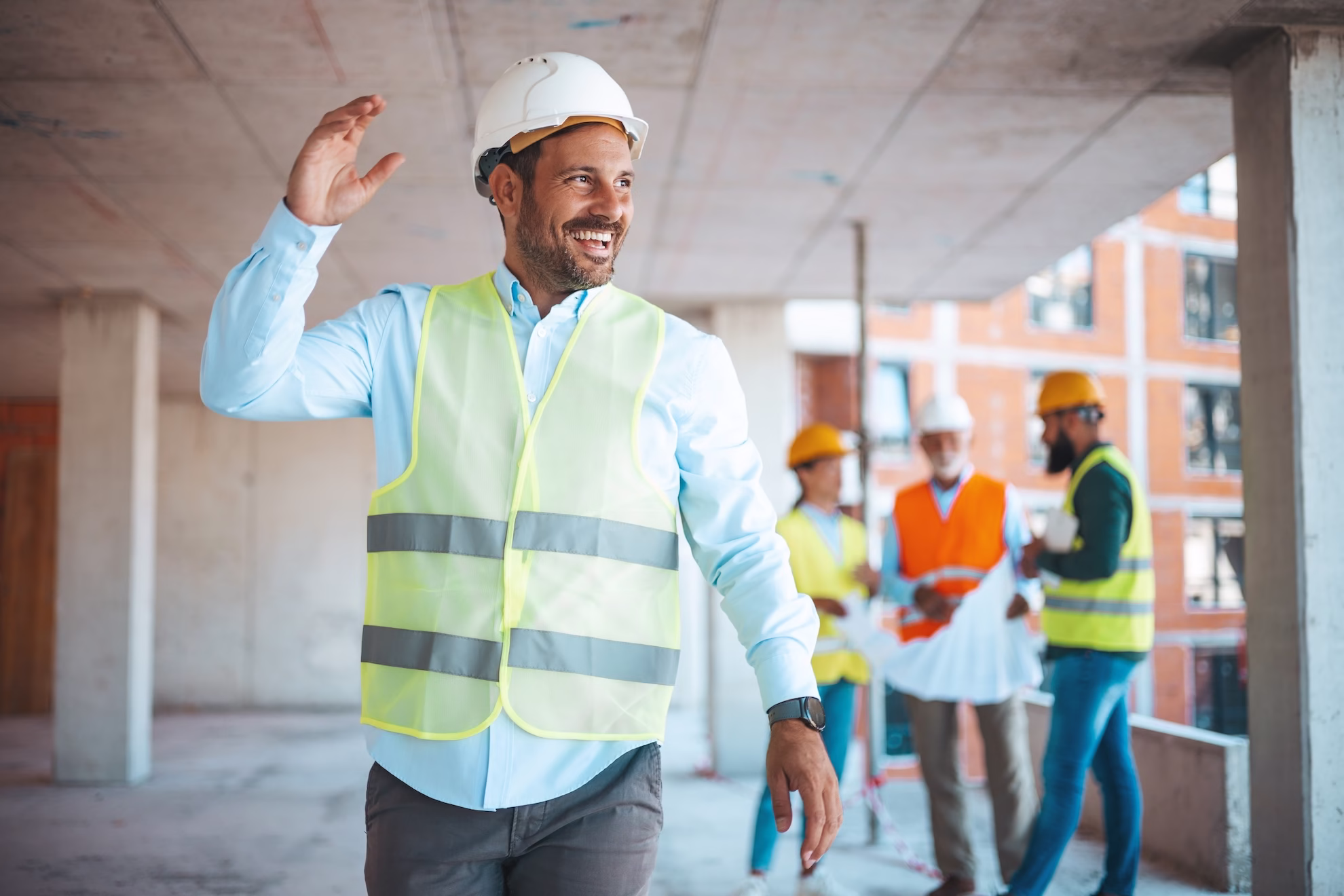 Man går iväg och hälsar med tre personer i bakgrunden på byggarbetsplats